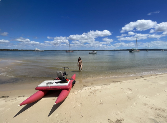Red waterbike on a sunny beach overlooking anchored boats and coastal waters